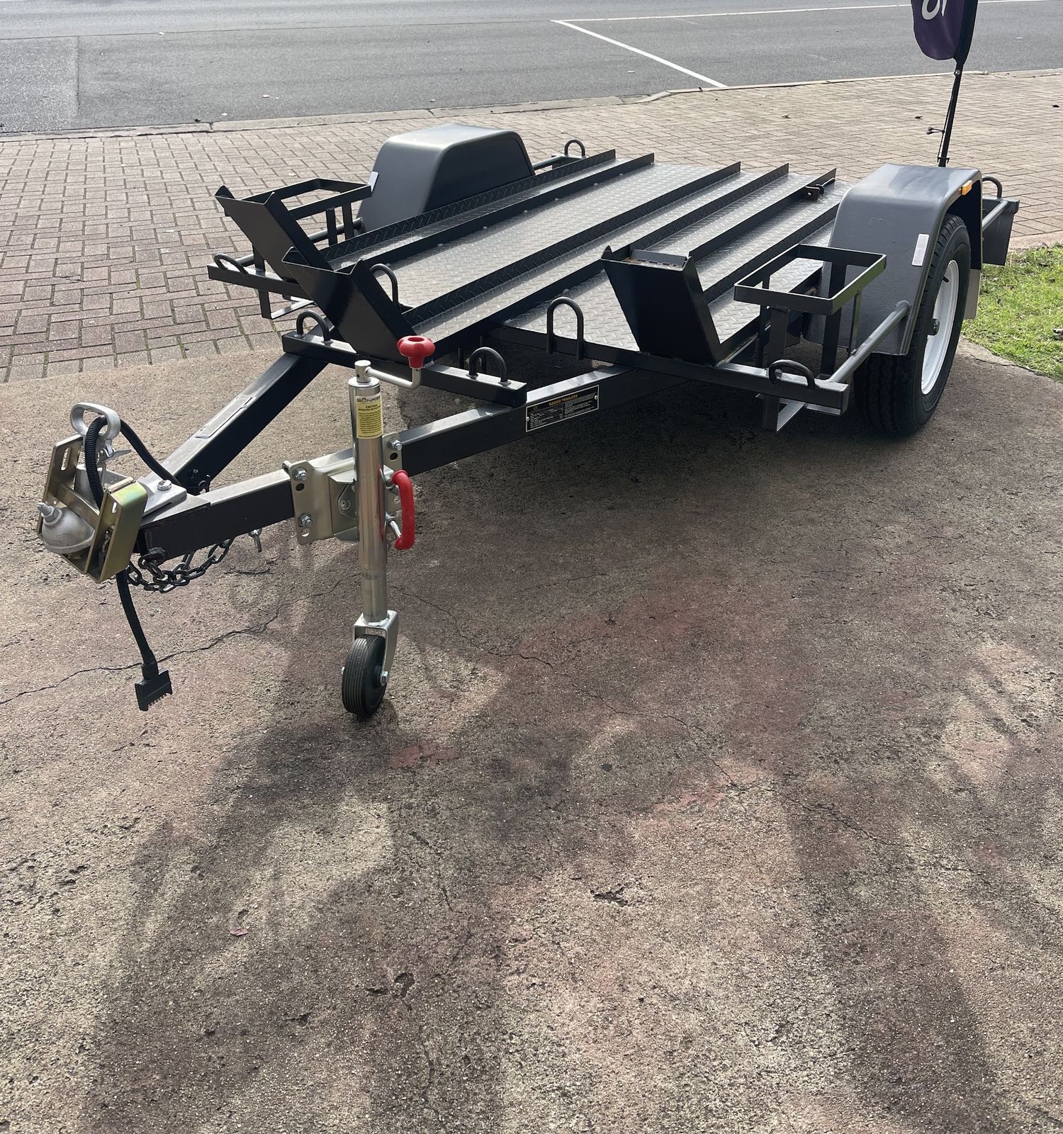 Single axle bike trailer with three rails and wheel chocks, parked on the kerb