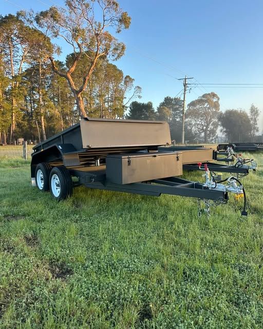 Tandem hydraulic tipper trailer with a sand coloured tub, parked in a paddock at dusk